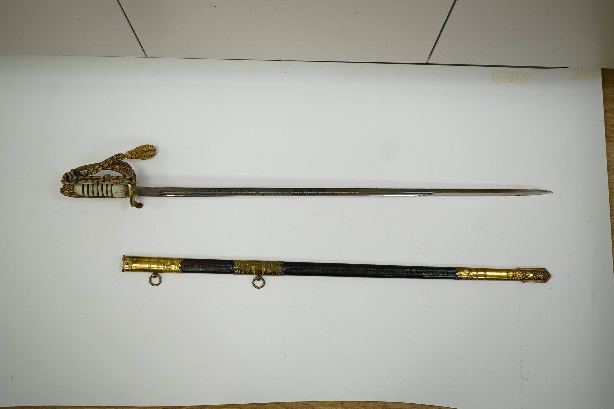 An 1846 pattern naval officer’s sword by Gieves, with folding thumb guard and knot, in its leather scabbard with brass mounts. Together with its outer soft leather cover. Condition - fair, notable wear to grip.